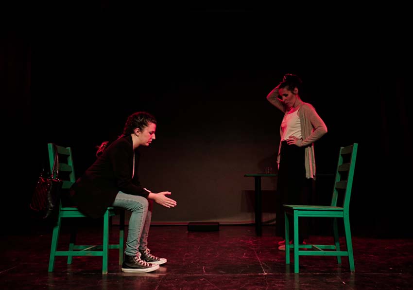 Una dona asseguda i una altra dempeus en l'escenari
